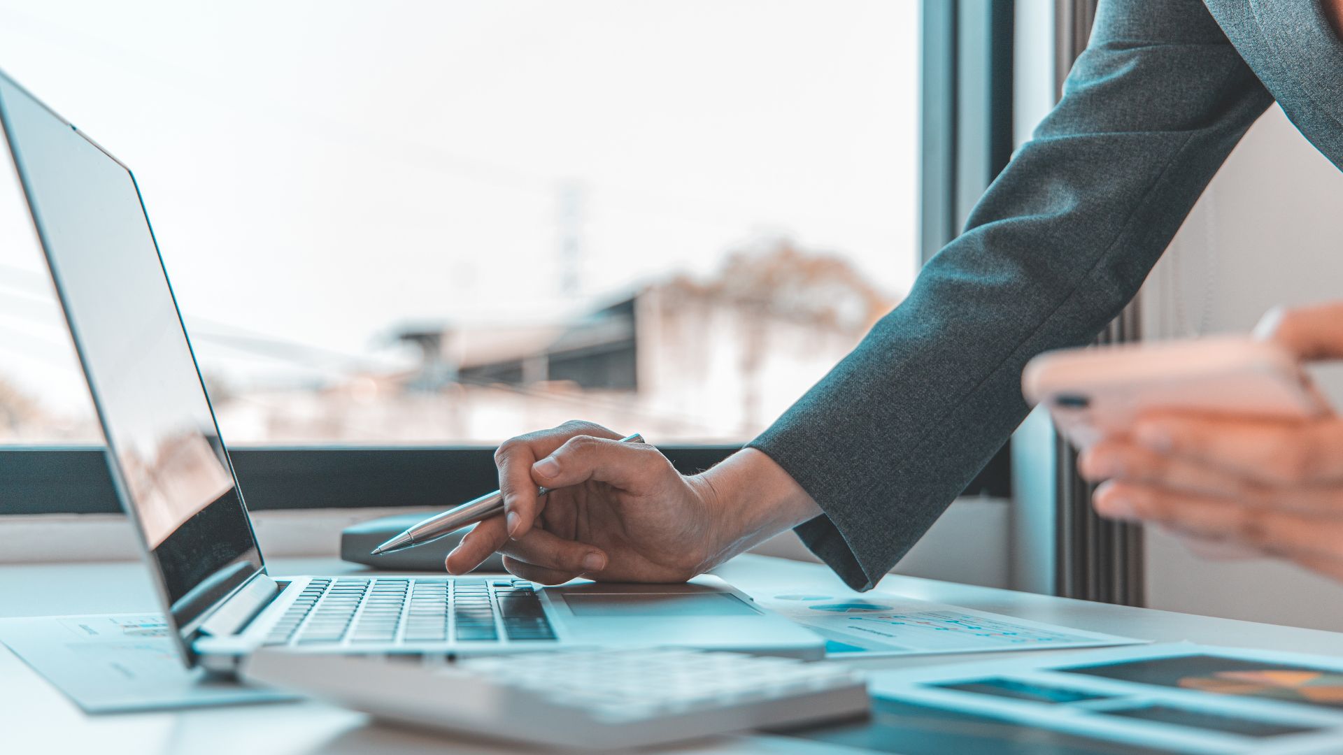 Schreibtisch mit Laptop und Frauenhand mit einem Kugelschreiber