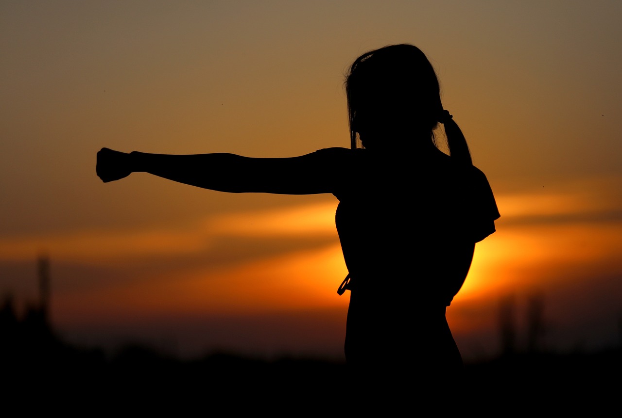Silhouette einer Frau, die vor Sonnenuntergang mit der Faust in die Luft schlägt